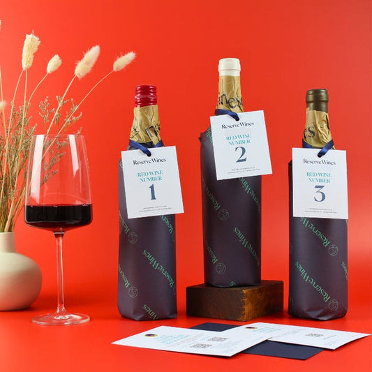 Three bottles of wine with decorative paper and a glass of red wine on a red background