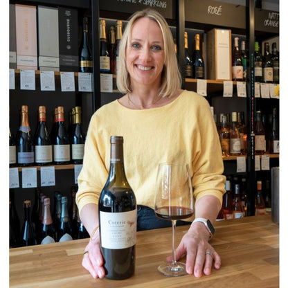 Kate Goodman holding a bottle of Coterie Cabernet Franc Malbec red wine and a glass in a wine store.