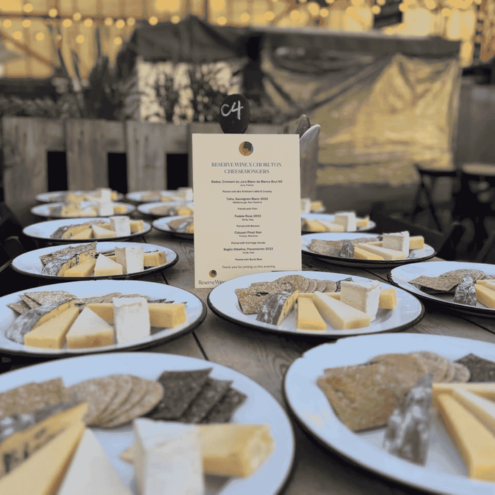 A table set up for a wine and cheese tasting event with multiple plates of cheese and a menu in the center.